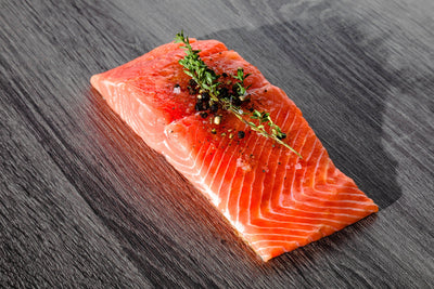 Angled close-up of Wild Alaskan king salmon fillet with visible marbling and sprig of thyme on dark wood