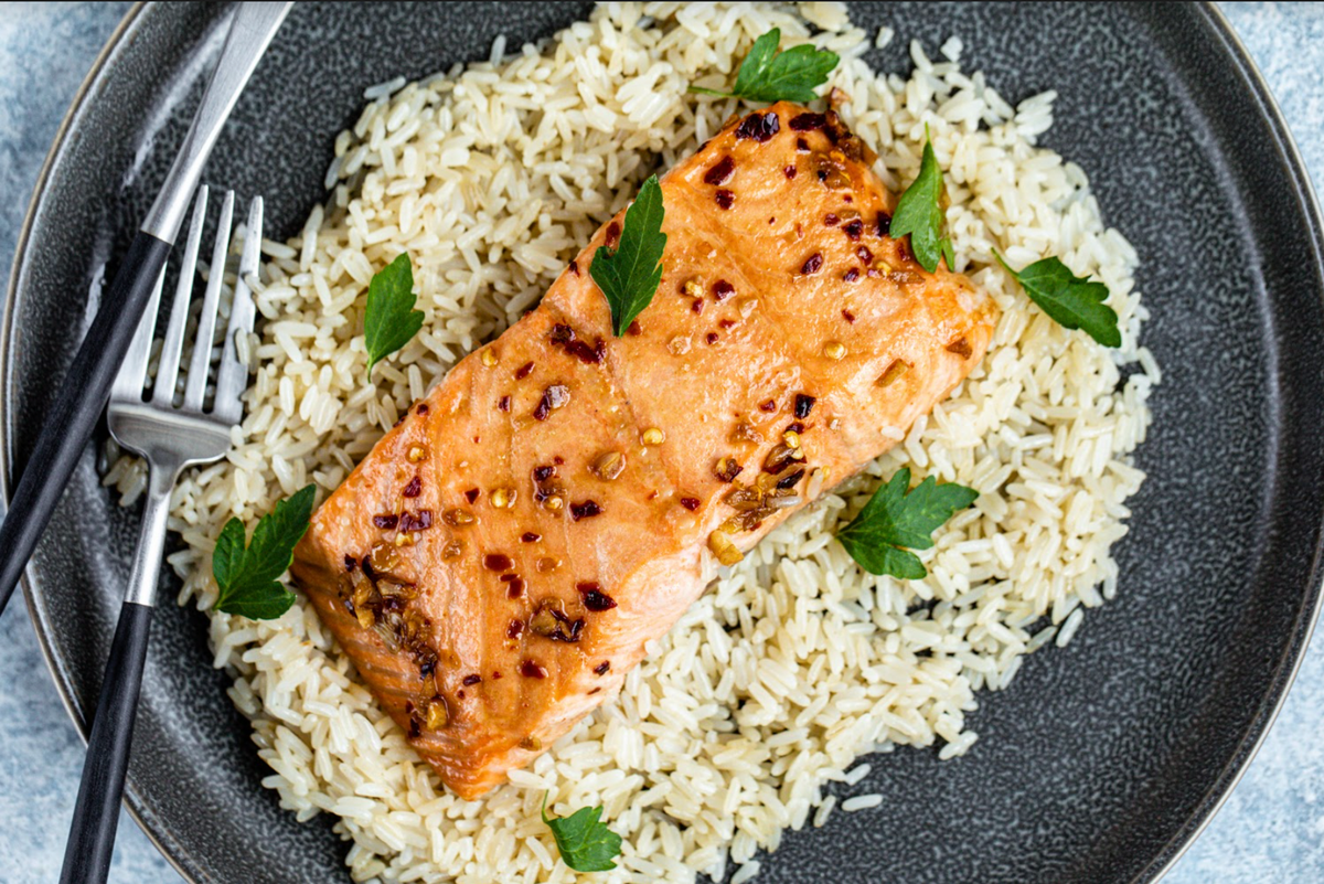 Seared wild sockeye salmon fillet with red pepper flakes and garlic on bed of white rice, parsley garnish