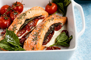Close view of two Caprese stuffed salmon fillets showcasing mozzarella, sun-dried tomatoes, and basil in a white baking dish