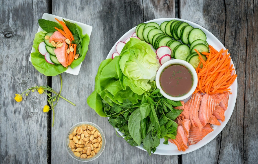 Top view of pan-fried salmon lettuce wraps showcasing lettuce, salmon, cucumber, carrots, radishes, and dipping sauce