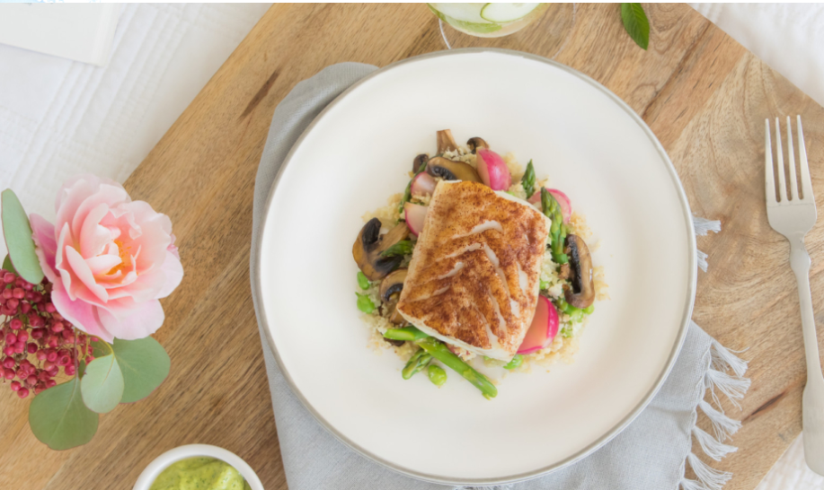 Seared white fish fillet with golden crust on couscous, asparagus, radishes and mushrooms on white plate