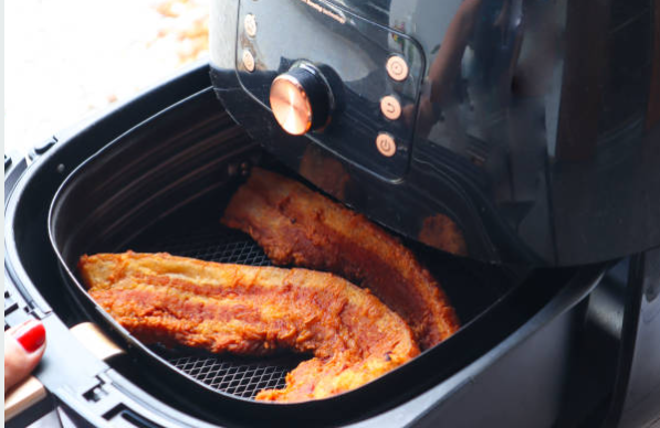 Hand removing air fryer basket containing breaded fish fillets