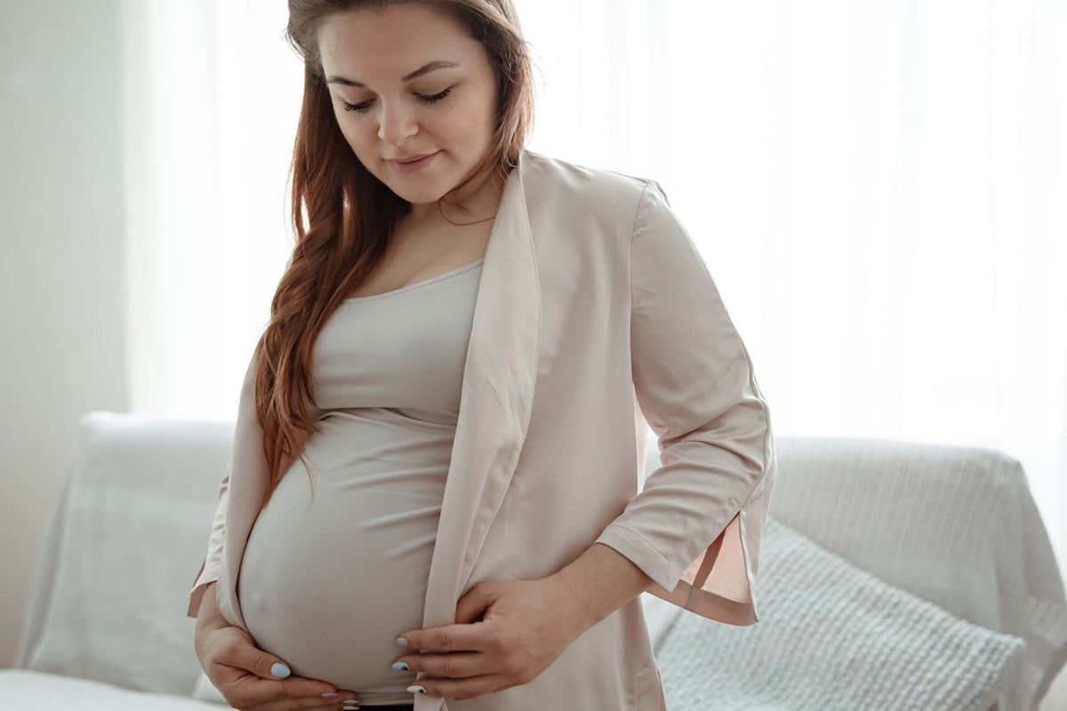 Pregnant woman gently cradling her belly in a softly lit living room