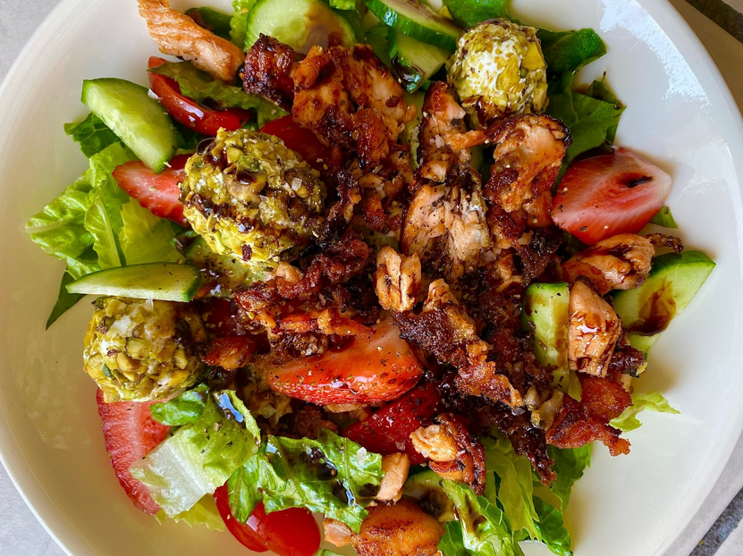 Salad with crispy salmon, strawberries, cucumber, lettuce, and pistachio-coated cheese balls