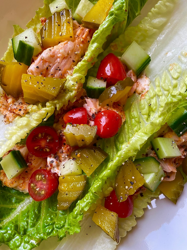 Romaine lettuce boats with flaked salmon, halved cherry tomatoes, diced cucumber and pickles, topped with cracked black pepper
