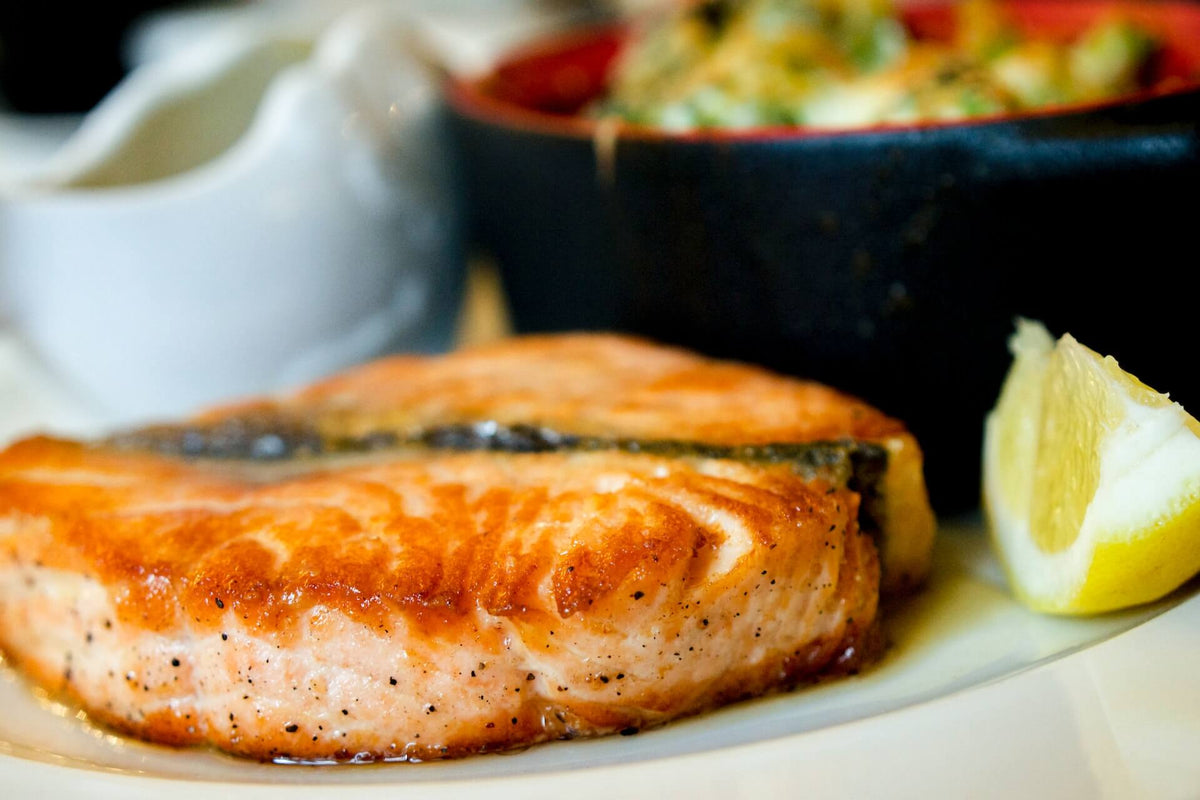 Air fried Alaskan salmon fillet on a plate with a lemon wedge and a sauce dish in the background