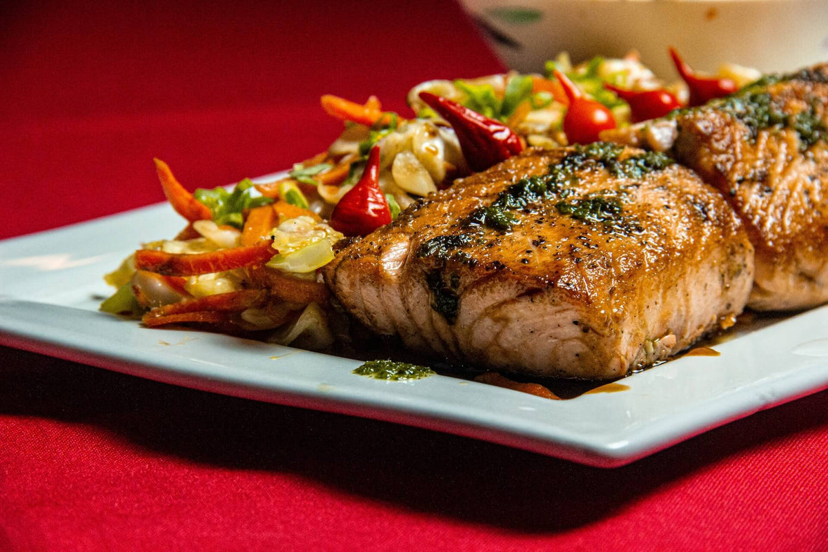 Two seared salmon fillets served with sautéed vegetables and small red chilies on a white plate