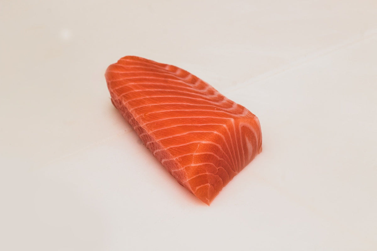 Close-up of raw sockeye salmon fillet showcasing bright red flesh and white fat striations on a white cutting board