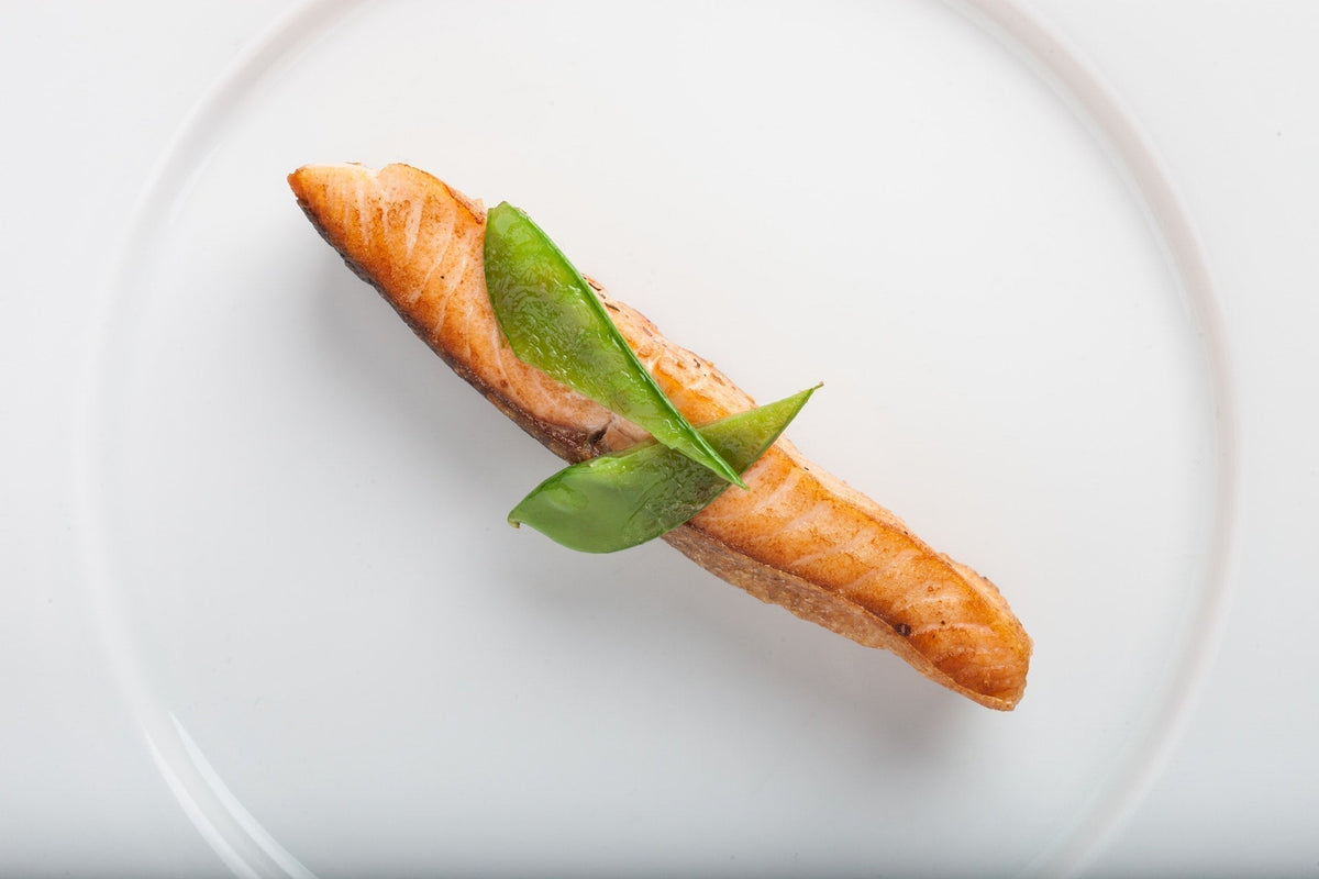 Top-down view of seared salmon fillet showcasing golden crust and pea garnish on a white plate