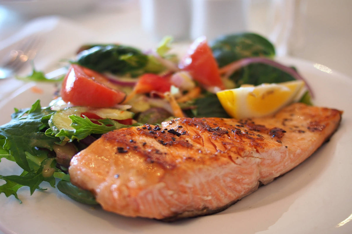 Seared Alaskan salmon fillet served with mixed salad and lemon wedge on a white plate
