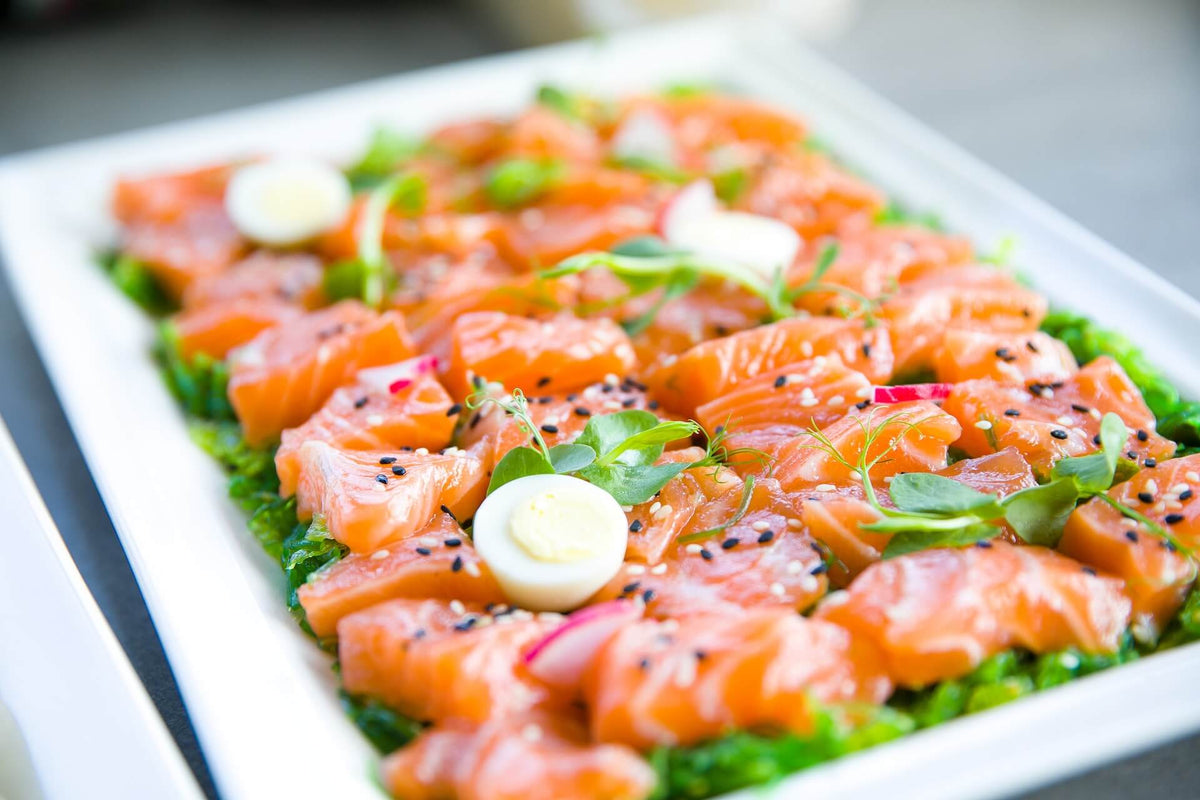 Raw salmon pieces garnished with herbs, sesame seeds, and quail eggs on a white platter