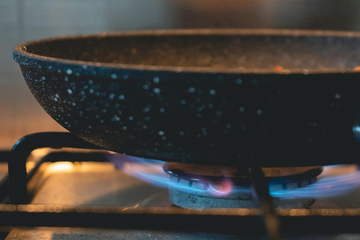 speckled frying pan heating on a gas stove burner with blue flame
