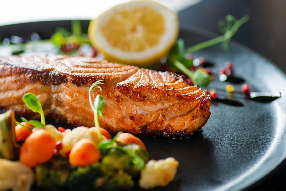 Grilled salmon fillet with lemon half and roasted vegetables on a black plate