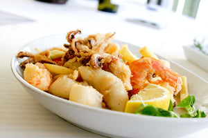 Close-up of fried mixed seafood (shrimp, calamari, battered fish) with lemon wedges and greens on a white ceramic plate