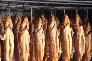 Close-up of smoked trout hung on metal hooks showcasing glossy golden-brown skin inside a smoker
