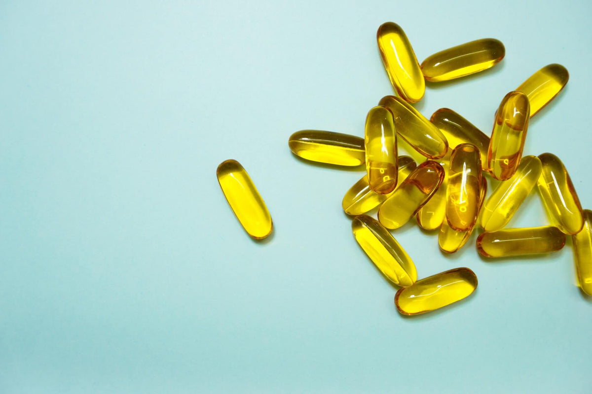 Yellow translucent omega-3 softgel capsules scattered on pale blue background, cluster at right