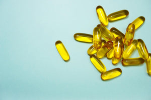 Yellow translucent omega-3 softgel capsules scattered on pale blue background, cluster at right
