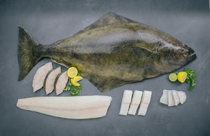 Whole halibut fish with sliced pieces, lemon, lime, and parsley on a gray surface
