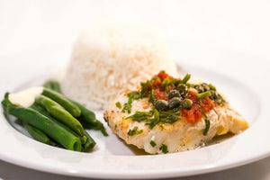 Cooked cod fillet with capers and herbs, served with green beans and white rice on a white plate