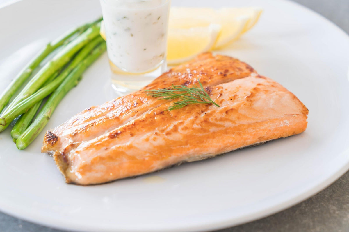 Baked salmon fillet served with roasted asparagus, lemon wedges and herb sauce on a white plate