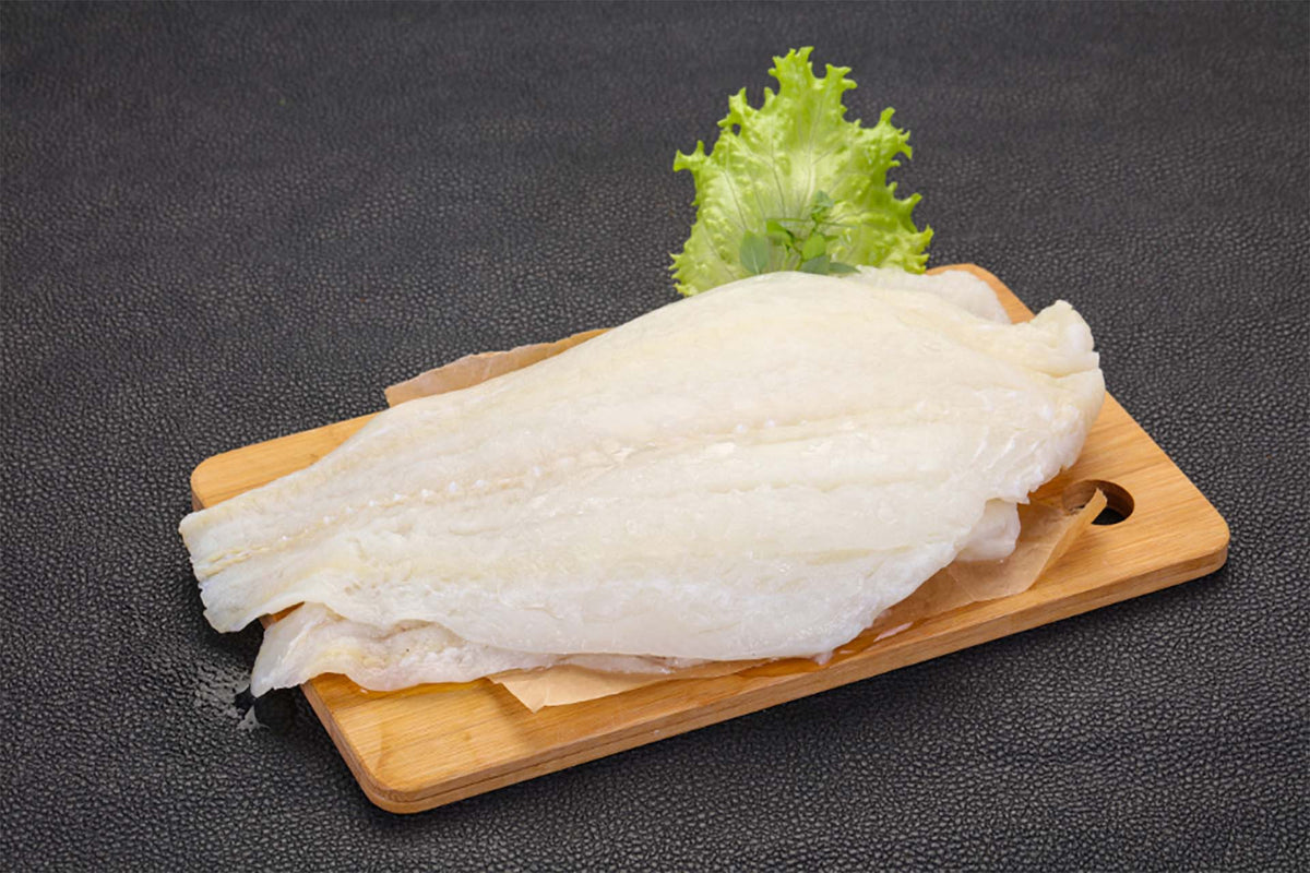 Raw halibut fillet on a wooden cutting board with green lettuce garnish