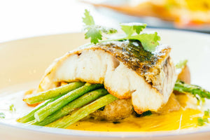 Cooked halibut fillet on green beans with sauce and a garnish on top