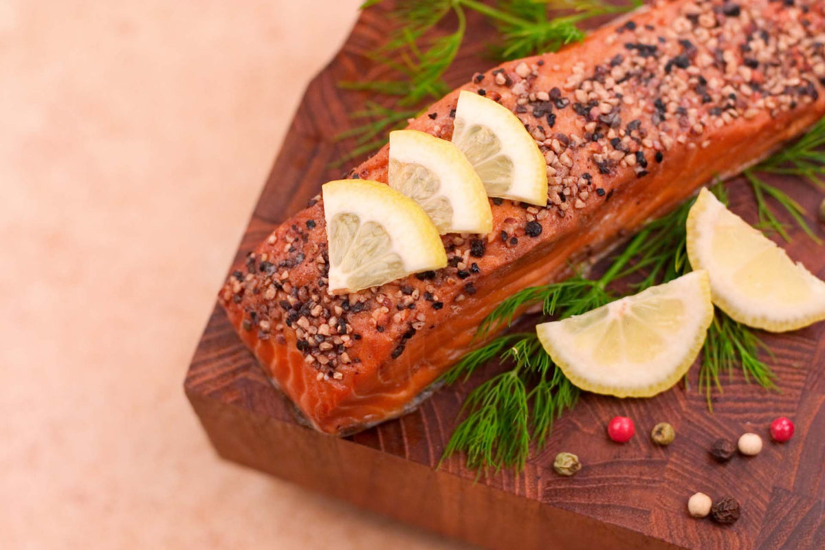 Seasoned wild sockeye salmon fillet with crushed pepper and lemon slices on wooden board garnished with dill