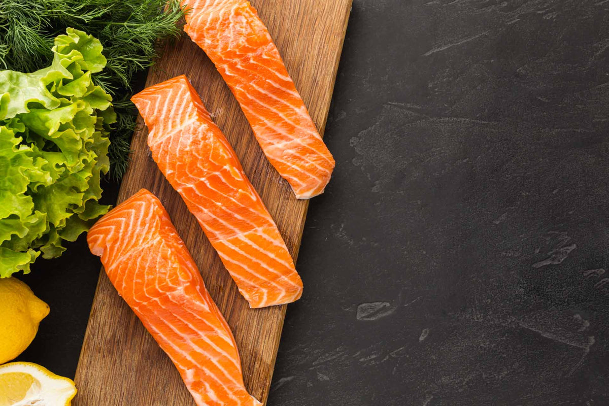 three raw salmon fillets on a wooden board with lettuce and lemon wedges