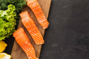 three raw salmon fillets on a wooden board with lettuce and lemon wedges