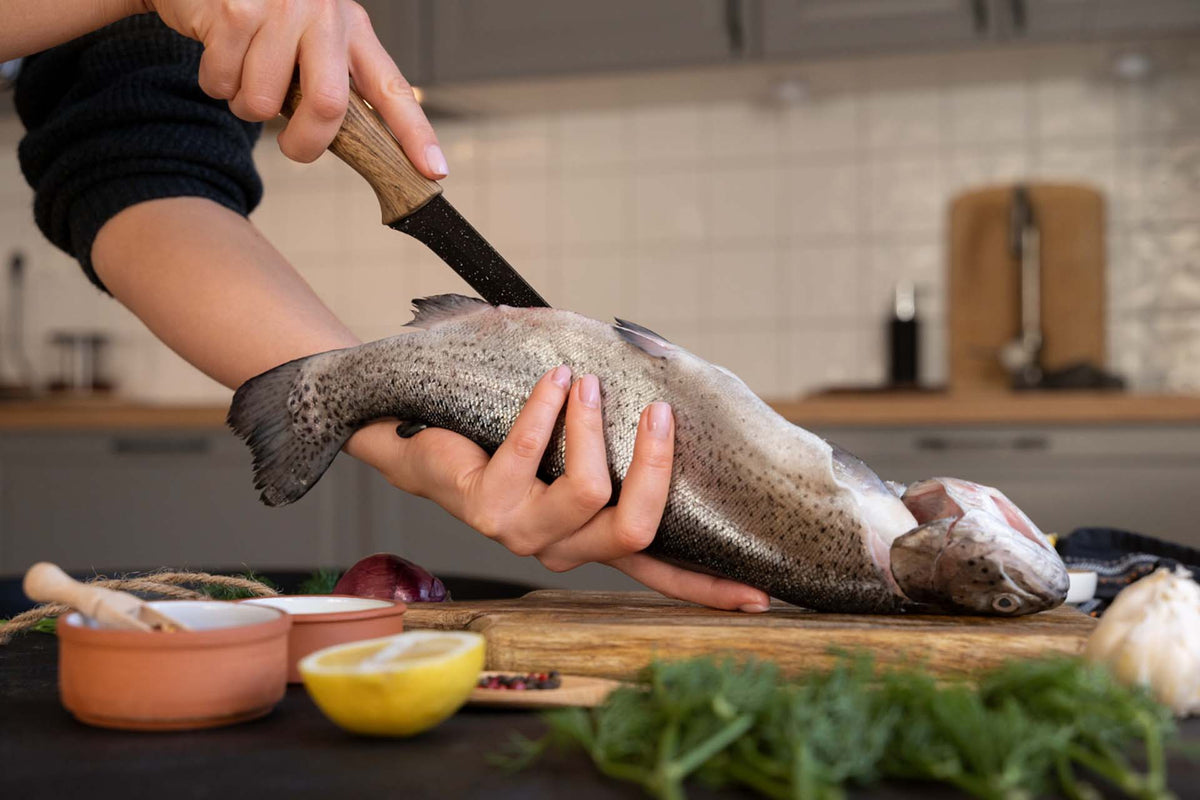 Hands filleting a whole salmon with a wooden-handled fillet knife over a kitchen cutting board