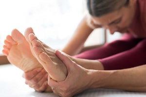 Person seated and holding their feet in a forward stretch, illustrating foot pain and discomfort related to gout
