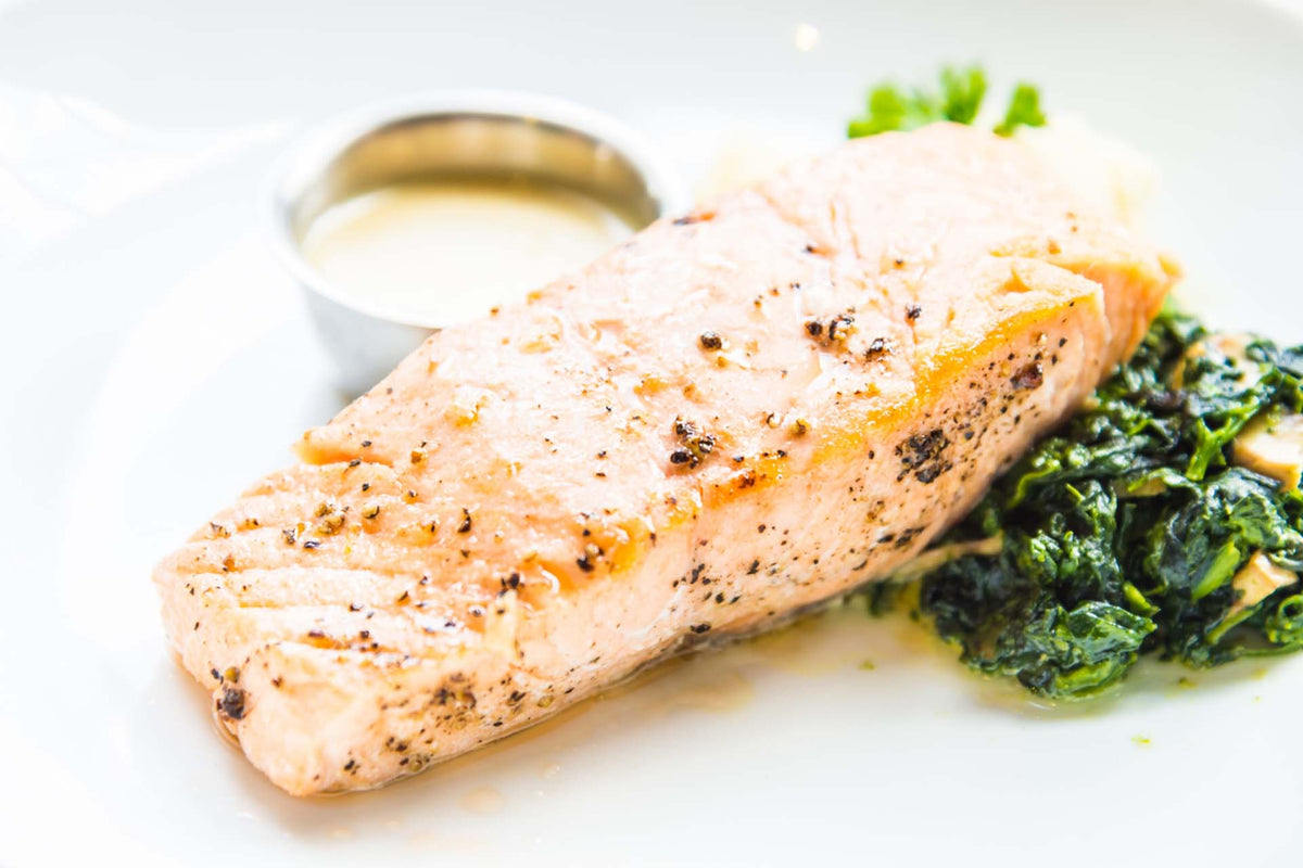 Poached Alaskan salmon fillet served on sautéed spinach with a small metal cup of lemon-butter sauce