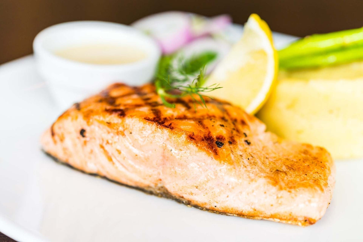 Pan-seared Alaskan sockeye salmon plated with lemon wedge, asparagus and a small sauce cup on a white plate