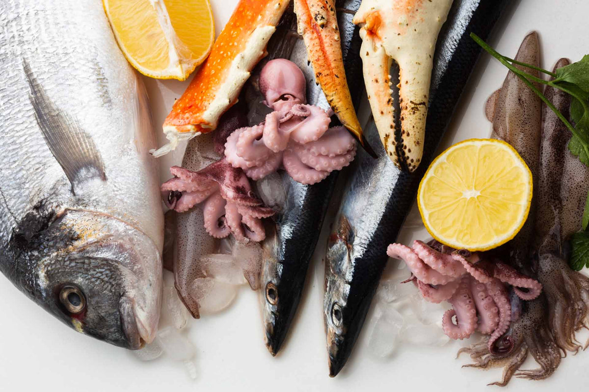 Raw seafood on ice labeled as high-cholesterol examples: whole fish, king crab claws, octopus, squid, and lemon halves