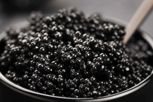 High-angle close-up of black caviar showcasing glossy, pearl-like eggs in a dark bowl