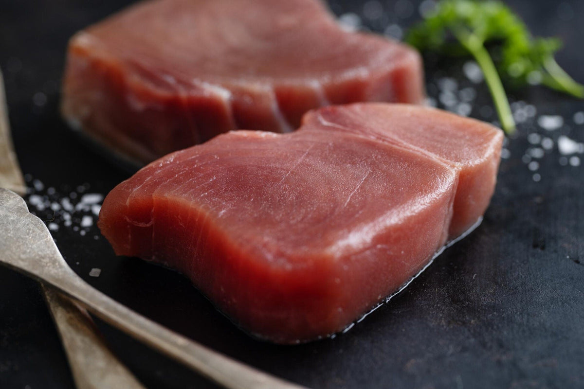Close-up of raw tuna steaks showing deep red color and firm, moist texture on dark slate with sea salt and parsley