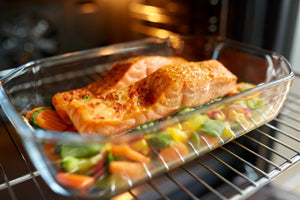 Two seasoned salmon fillets on mixed vegetables in a glass baking dish inside an oven
