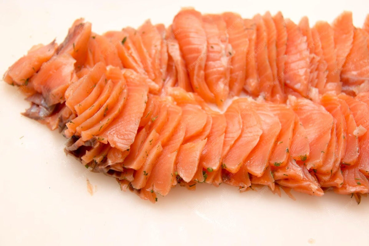 Close-up of thinly sliced cured Alaskan salmon with dill flecks on a white cutting board