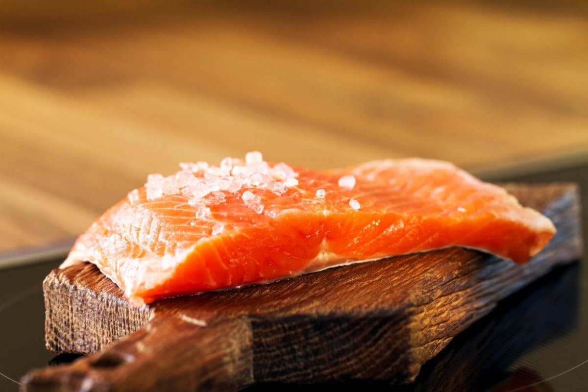 Close-up side view of raw sockeye salmon fillet sprinkled with coarse salt on a wooden cutting board