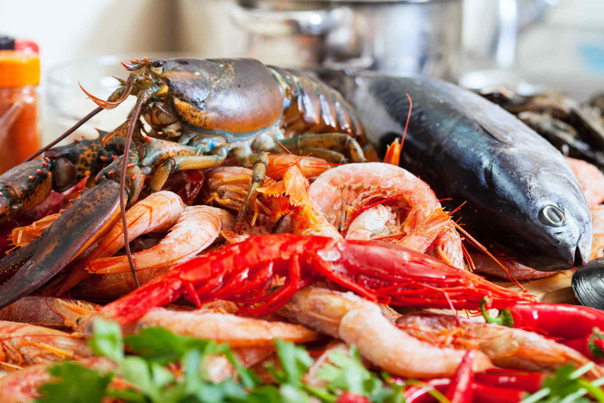 Assorted seafood on display: lobster with claws, whole fish, shrimp and red prawns with parsley and chili.