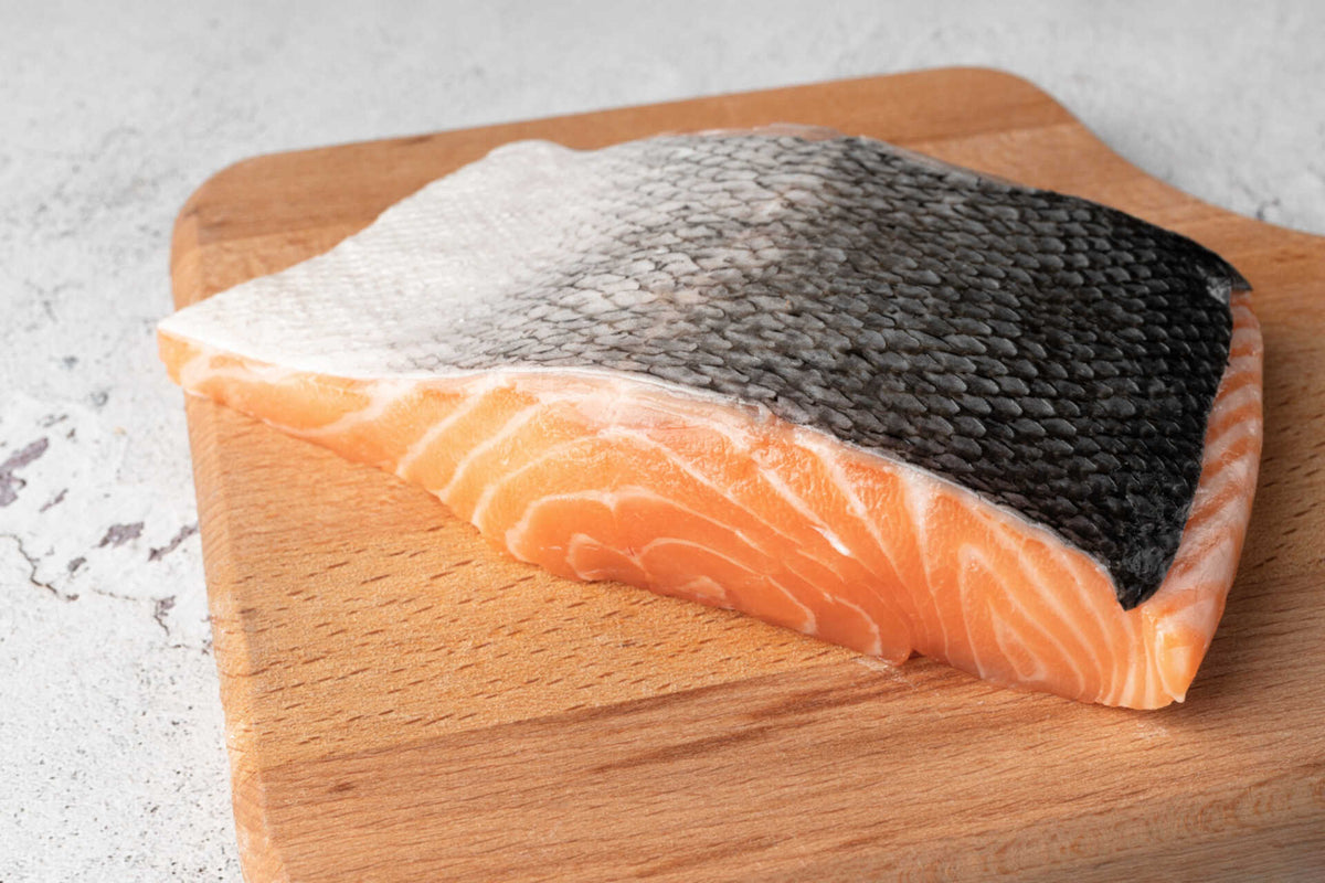 Close-up of salmon fillet with skin on showcasing pink flesh and scale texture on a wooden cutting board