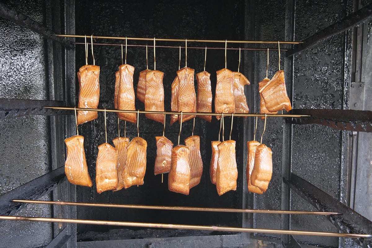 Smoked salmon fillets hanging on metal hooks inside a smoker