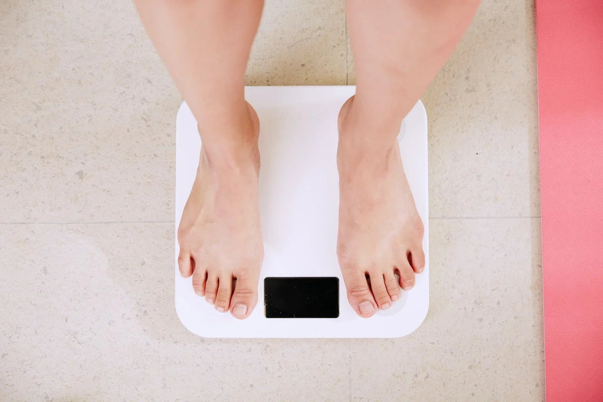Bare feet standing on a digital bathroom scale on a tiled floor next to a pink exercise mat