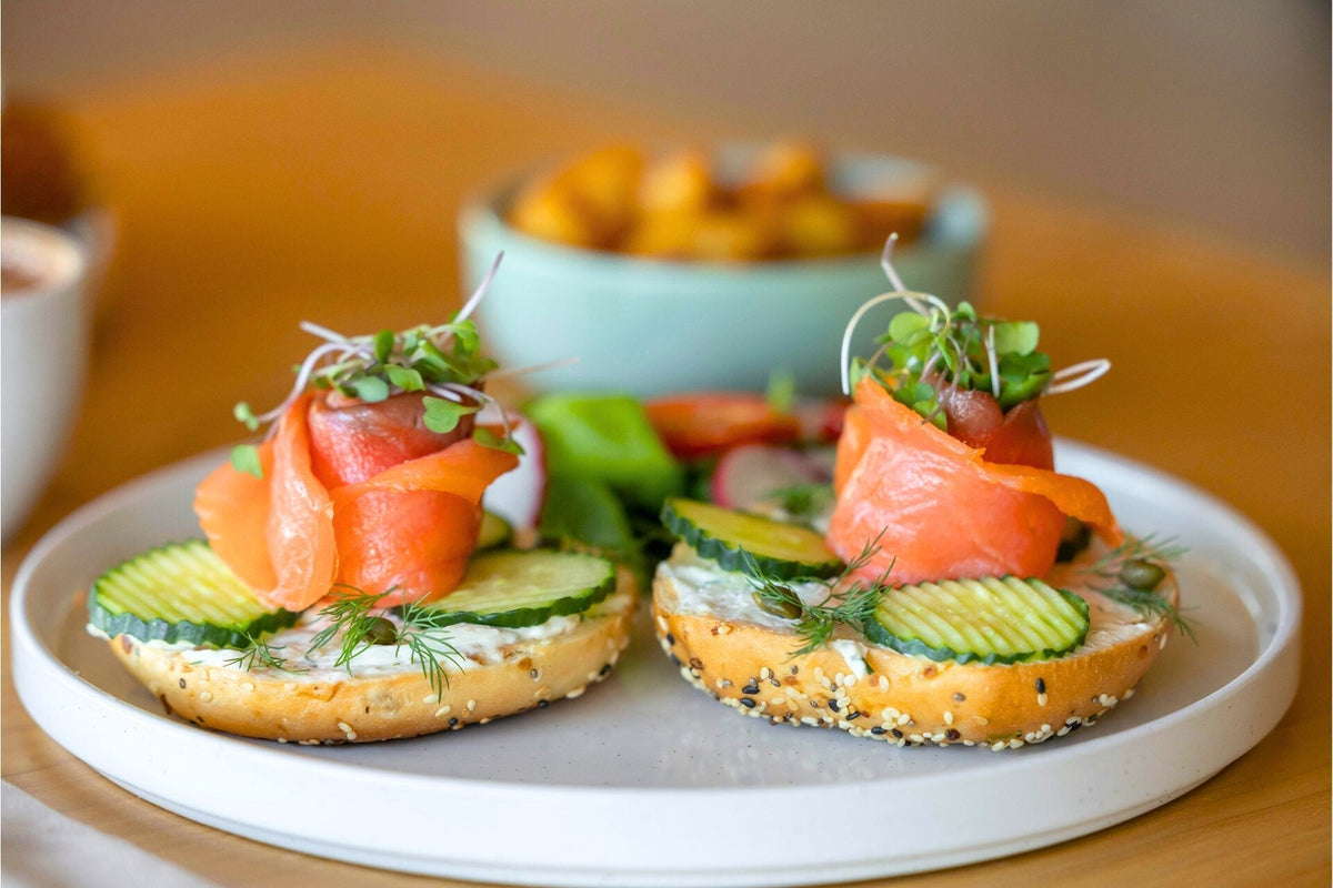 Bagel halves with cream cheese, cucumber, dill and Alaskan smoked salmon rosettes topped with microgreens, blurred bowl