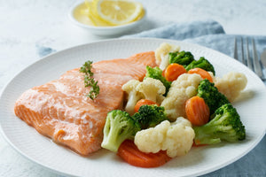 Oven-baked salmon fillet served with steamed broccoli, cauliflower, and carrots on a white plate
