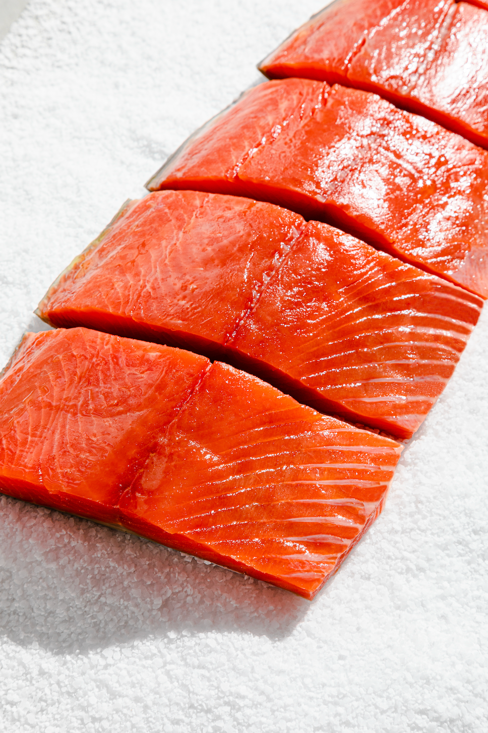 Four raw wild sockeye salmon portions laid in a line on crushed ice