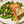 Seared salmon fillet with sugar snap peas, blanched radishes and pea-studded compound butter on a white plate.