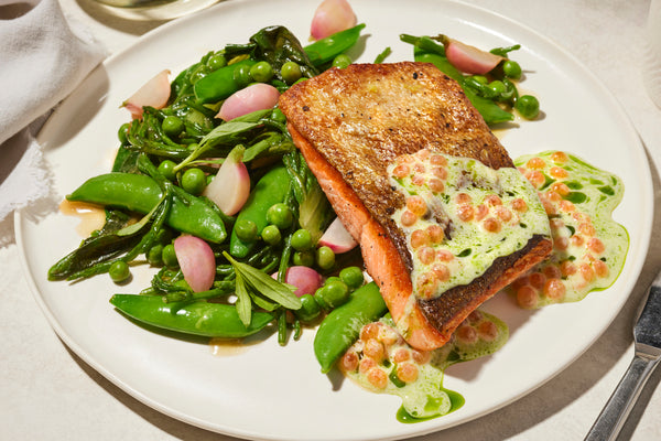 Seared salmon fillet with sugar snap peas, blanched radishes and pea-studded compound butter on a white plate.