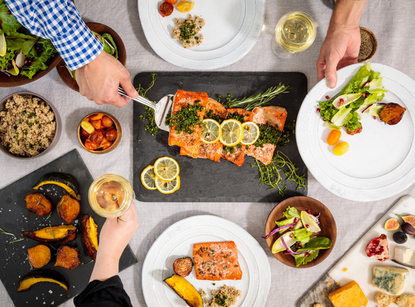 Overhead view of a dinner table with salmon topped with lemon slices, roasted potatoes, salad and a glass of white wine