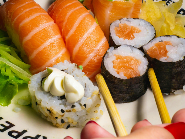 Salmon nigiri, salmon maki rolls, and a sushi roll with cream cheese and sesame seeds on a plate with chopsticks